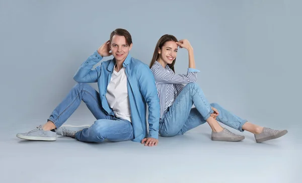 Pareja joven en jeans elegantes sentados sobre fondo gris — Foto de Stock
