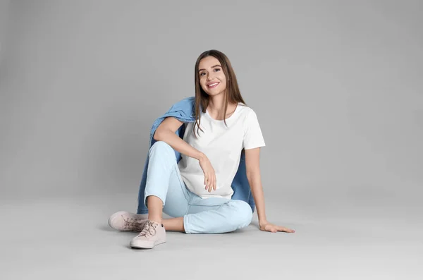 Молодая женщина в стильных джинсах сидит на сером фоне — стоковое фото