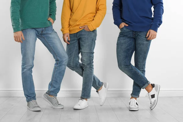 Grupp av unga män i snygga jeans nära vit vägg, närbild — Stockfoto