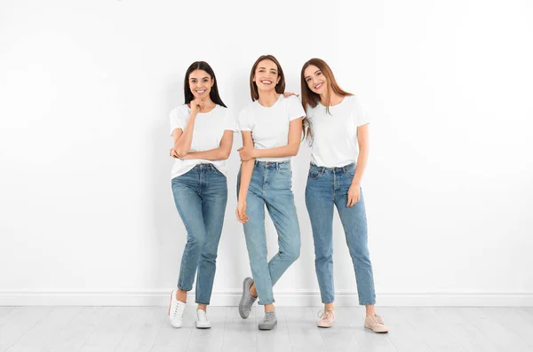 Grupo de mulheres jovens em jeans elegantes perto da parede branca — Fotografia de Stock
