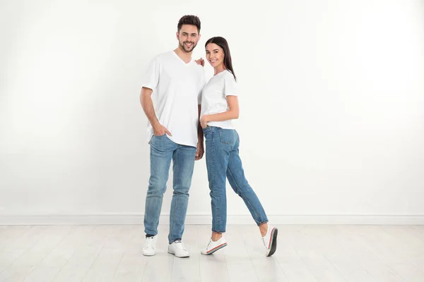 Jong stel in stijlvolle jeans bij witte muur — Stockfoto