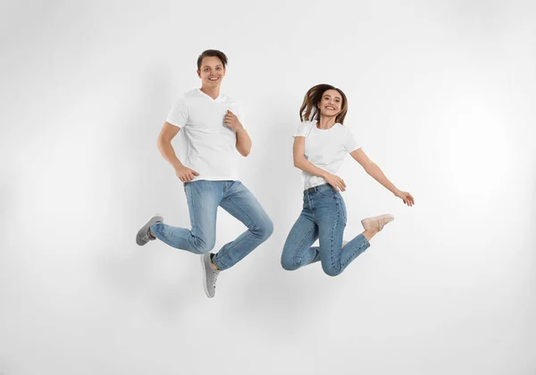 Pareja joven en jeans elegantes saltando cerca de la pared blanca — Foto de Stock