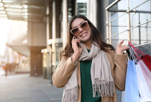 Alışveriş torbalarıyla güzel genç bir kadın akıllı telefondan konuşuyor. — Stok fotoğraf