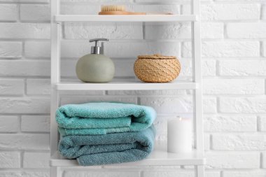 Beyaz tuğla duvarın yanındaki raflarda temiz havlu ve sabun makinesi var.