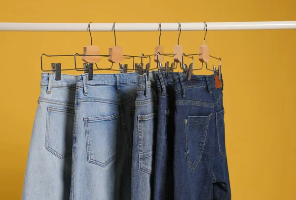 Bastidor con diferentes pantalones vaqueros sobre fondo amarillo — Foto de Stock