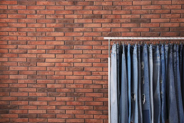 Rack med snygga jeans nära tegelvägg. Plats för text — Stockfoto