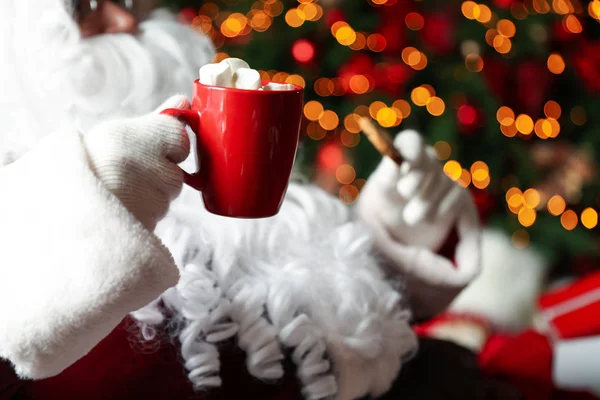 Weihnachtsmann Mit Heißgetränk Und Plätzchen Gegen Verschwommene Weihnachtsbeleuchtung Nahaufnahme — Stockfoto