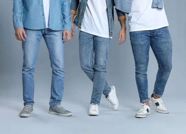 Група молодих чоловіків у стильних джинсах на сірому фоні, крупним планом — стокове фото