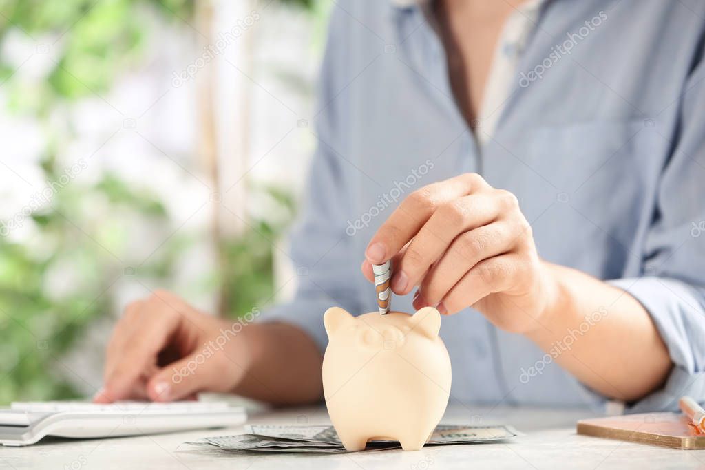 Woman putting money into piggy bank at table, closeup