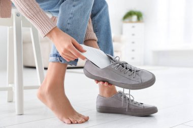 Woman putting orthopedic insole into shoe at home, closeup clipart