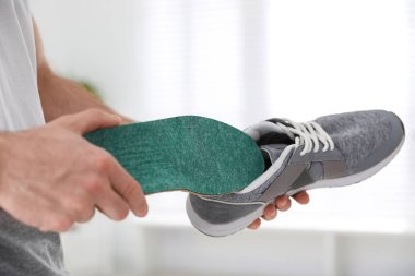 Man putting orthopedic insole into shoe at home, closeup clipart