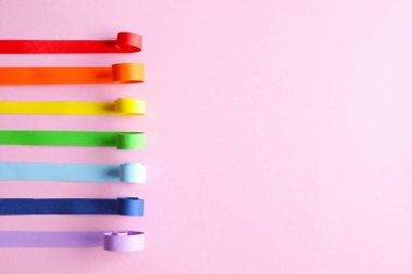 Parlak kağıt şeritler ve pembe arkaplan üzerine yazı için boşluk. Gökkuşağı renkleri