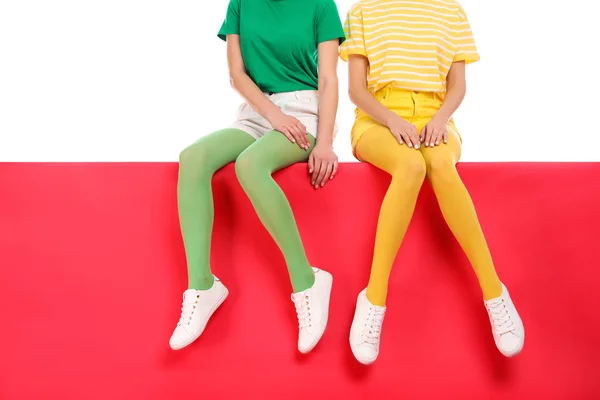 Mujeres con medias brillantes sentadas juntas sobre fondo de color — Foto de Stock