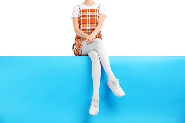 Woman wearing white tights and stylish shoes sitting on color ba — 스톡 사진