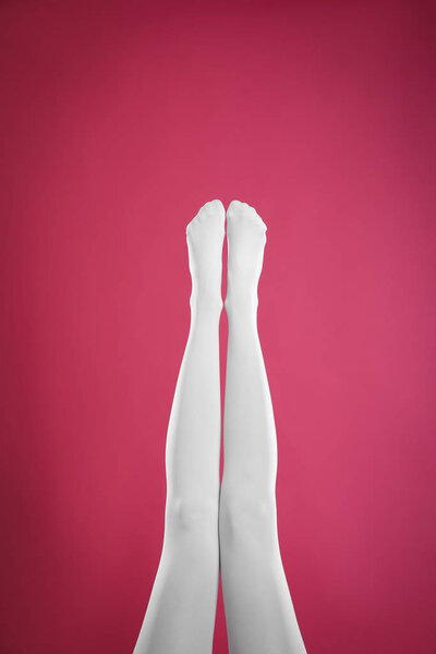 Woman wearing white tights on crimson background, closeup of legs