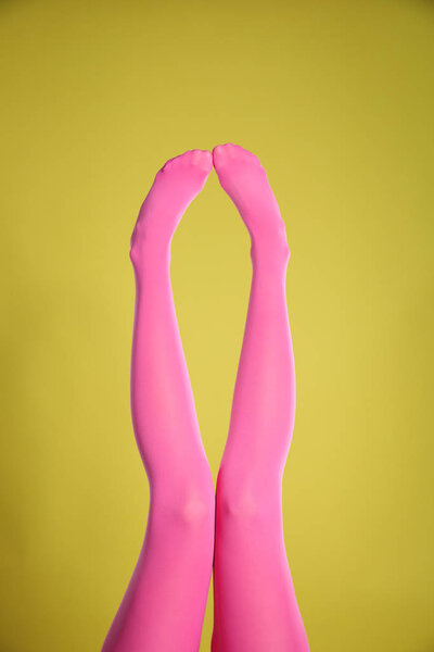 Woman wearing pink tights on yellow background, closeup of legs