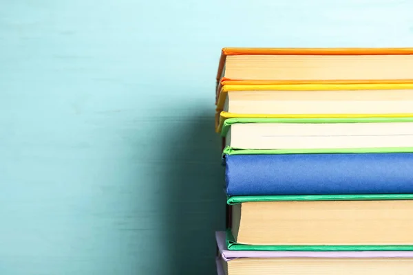 Stack of colorful books on light blue wooden background, closeup. Space for text