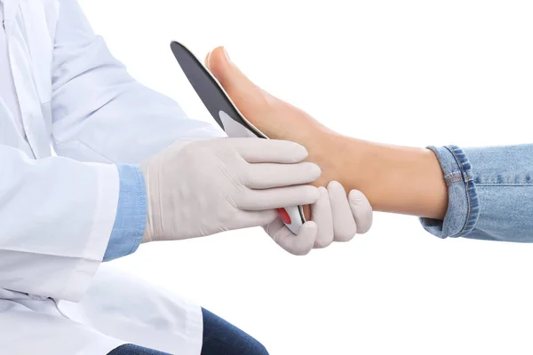 Мужчина ортопед, устанавливающий стельку на ногу пациента против белого — стоковое фото