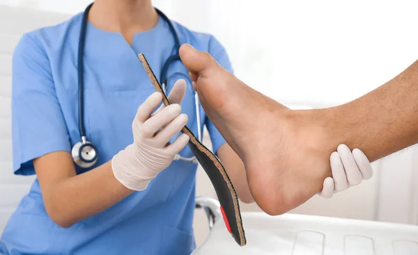 Female orthopedist fitting insole on patient's foot in clinic, c — Stock Photo, Image