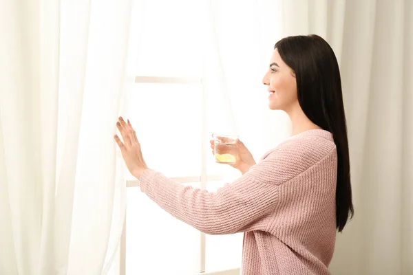 창가에서 맛있는 레몬 물을 마시고 있는 아름다운 젊은 여자 — 스톡 사진