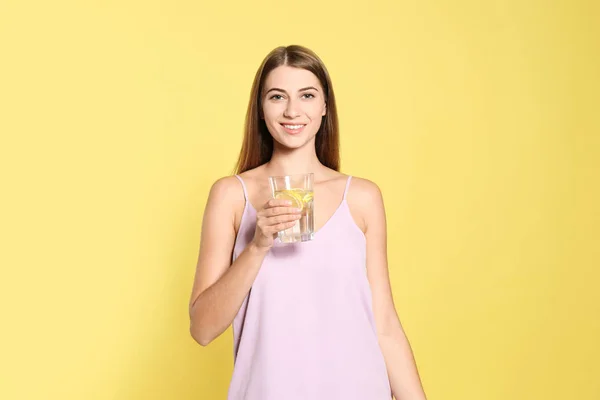 Mladá žena se sklenicí citrónové vody na žlutém pozadí — Stock fotografie