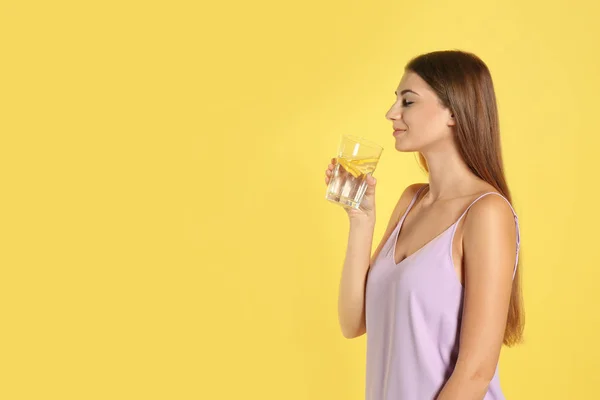 Jovem mulher bebendo água de limão no fundo amarelo. Espaço para — Fotografia de Stock