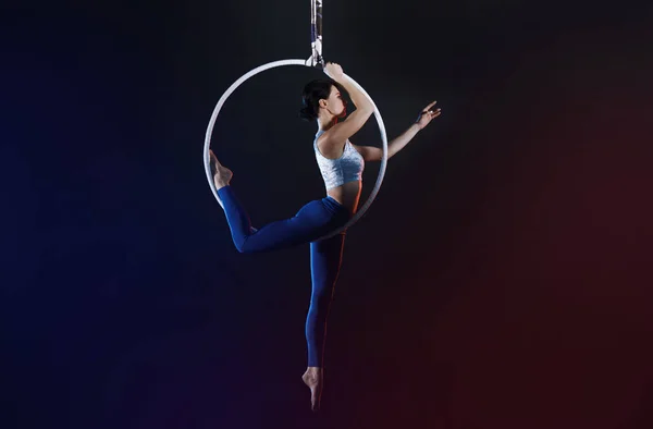 Mulher jovem realizando elemento acrobático no anel aéreo dentro de casa — Fotografia de Stock