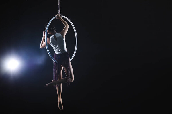 Young woman performing acrobatic element on aerial ring against 