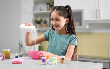 Sevimli küçük kız mutfaktaki masada kaseye tutkal döküyor. Diy.
