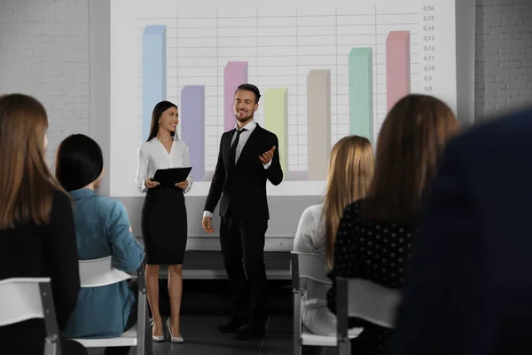 Business trainers giving lecture in conference room with projection screen