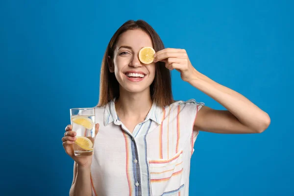 Jonge vrouw met glas citroen water op licht blauwe achtergrond — Stockfoto