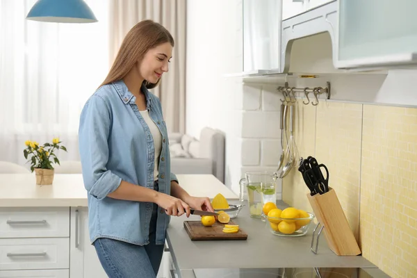 Jovem mulher cortando limão para refrescar bebida na cozinha — Fotografia de Stock