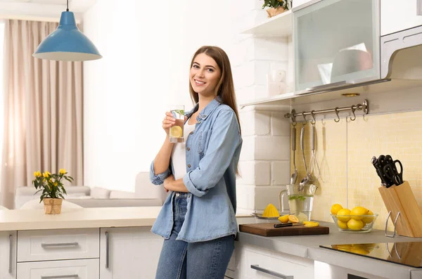 Mujer joven con vaso de agua de limón en la cocina — Foto de Stock