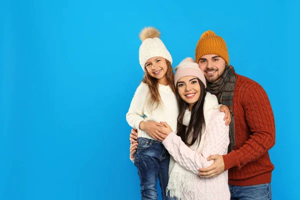 Happy family in warm clothes on blue background, space for text. Winter vacation