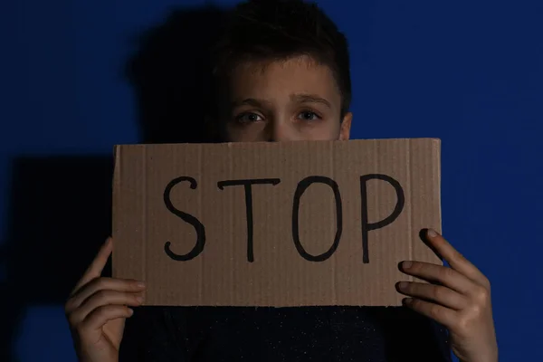 Maltratado niño pequeño con el signo PARADA cerca de la pared azul. Violen doméstica — Foto de Stock