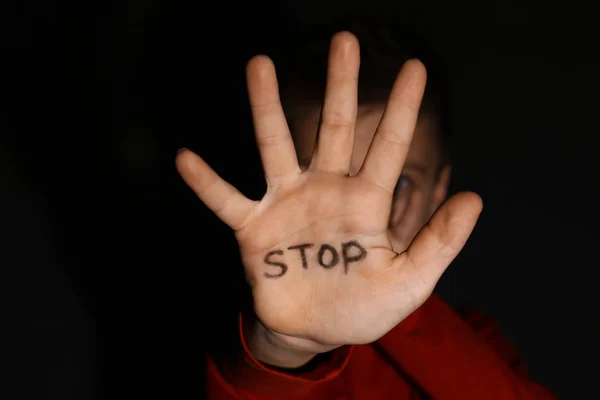 Niño abusado mostrando la palma de la mano con la palabra DETENER contra espalda negra — Foto de Stock