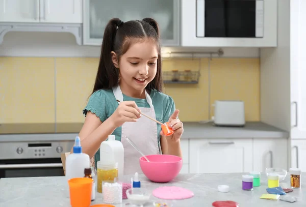 Милая маленькая девочка делает домашнюю грязную игрушку за столом на кухне — стоковое фото