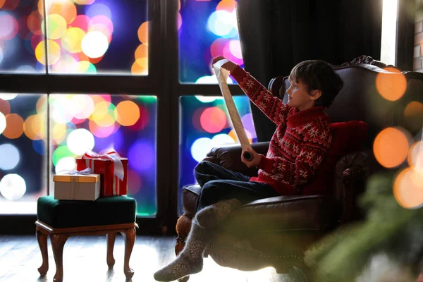 Petit garçon avec liste de souhaits au Père Noël près de la fenêtre à l'intérieur. Ch. — Photo
