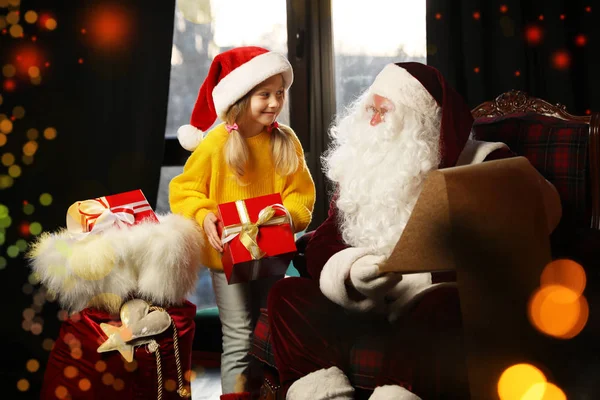 Little girl with Christmas gift near Santa Claus indoors — Stock Photo, Image