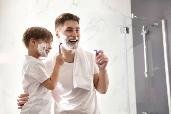 Dad and son with shaving foam on their faces having fun in bathr — ストック写真