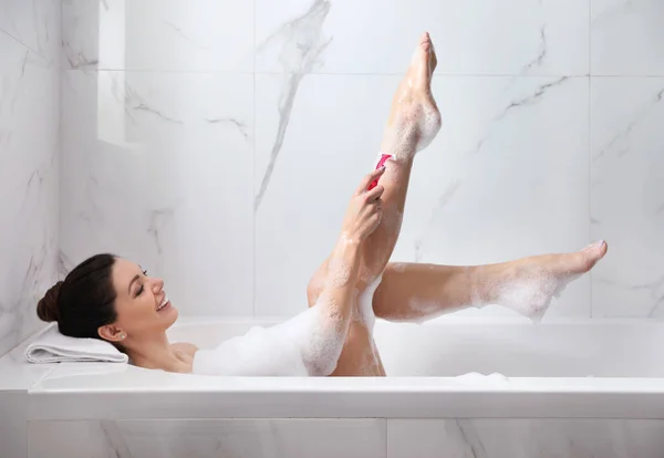 Mladá žena holení nohy, zatímco s bublinkovou koupel — Stock fotografie