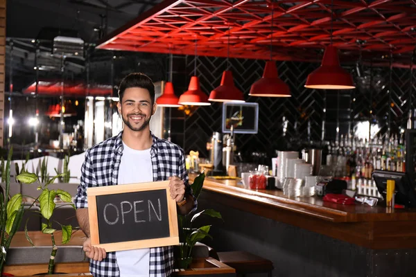 Young business owner holding sign OPEN in his cafe. Space for te