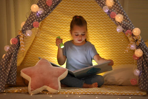 Dívka s baterkou čtení knihy ve stanu hrát doma — Stock fotografie
