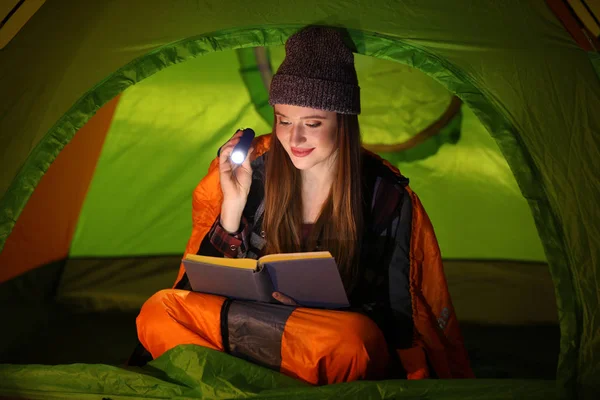 Giovane donna con torcia lettura libro in tenda — Foto Stock
