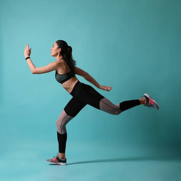 Jeune femme athlétique courant sur fond turquoise, vue latérale — Photo
