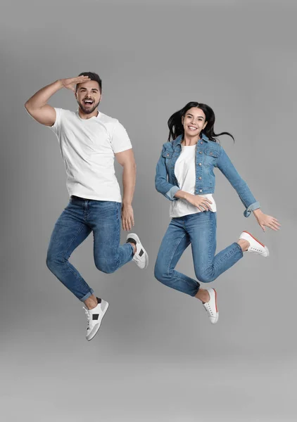 Jovem casal em jeans elegantes pulando em fundo cinza — Fotografia de Stock