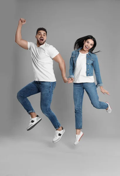 Jovem casal em jeans elegantes pulando em fundo cinza — Fotografia de Stock