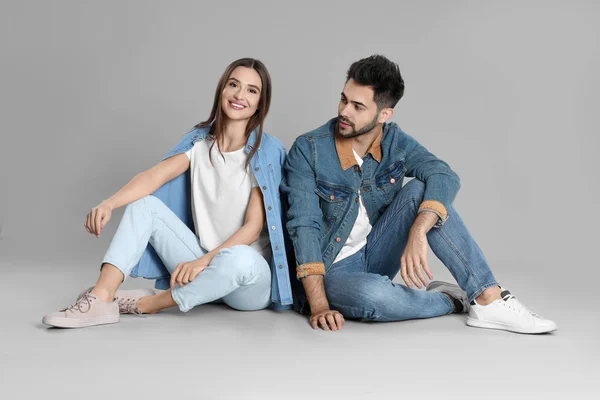 Jovem casal em jeans elegantes sentado no fundo cinza — Fotografia de Stock