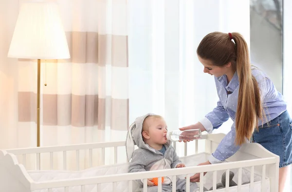 Teen nanny giving cute little baby water from bottle at home — 스톡 사진