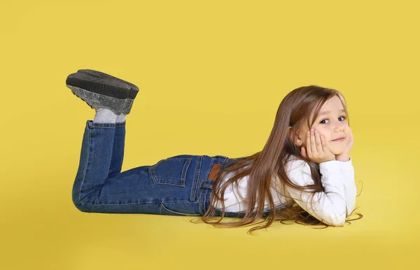 Симпатична дівчинка лежить на жовтому тлі — стокове фото